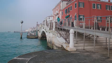Arched-bridge-over-Venetian-waterway,-misty-horizon