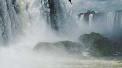 Close-Up-View-of-Slow-Motion-Iguacu-Falls-Waterfalls-in-Beautiful-Rainforest-Valley,-Mossy-Large-Rocks-Showered-in-Spray-From-Splashing-Falling-Water-From-Tall-Cliff-Edge-in-Brazil,-South-America
