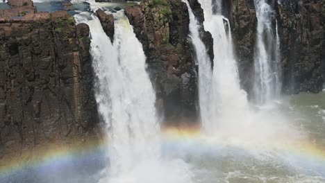 Slow-Motion-Tracking-View-of-Beautiful-Colourful-Group-of-Waterfalls-Eroding-Rock,-Falling-into-Beautiful-Rainbow-Pool,-Bright-Rainbow-in-Front-of-Amazing-Rocky-Waterfall-Landscape-in-Iguazu-Falls