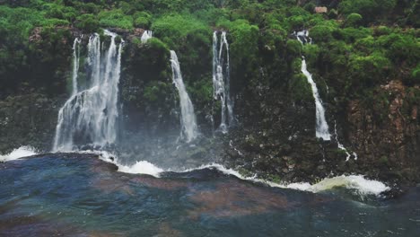 Iguazu-Falls-Slo-Mo-Waterfall-Stream-Falling-off-Huge-Cliff-into-Distant-Jungle-Rainforest-Landscape,-Tall-Greenery-Surrounding-Beautiful-Clear-Waterfall-Dropping-off-Tall-Cliff-Edge-in-Brazil