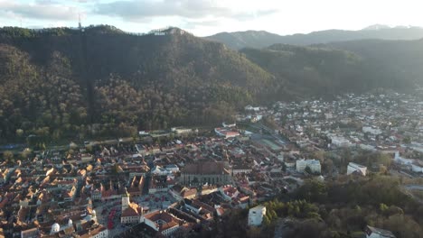 Aerial-shot-of-romania,-brasov-in-the-middle-of-the-mountains-of-green-trees-at-sunrise-or-sunset