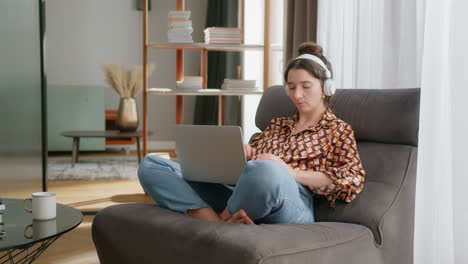 Girl-in-living-room-puts-on-headphones-and-connects-to-virtual-meeting