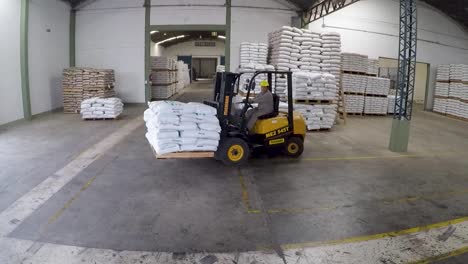 Forklift-operating-in-a-warehouse-with-stacked-sacks,-industrial-setting,-worker-in-action