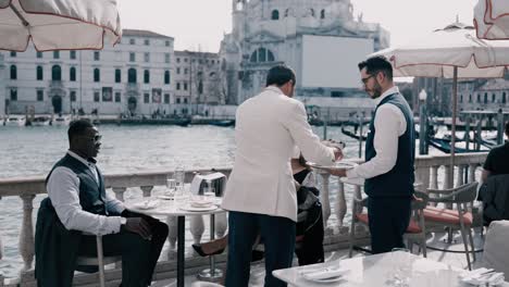 Stilvolles-Mixed-Race-Paar-Mit-Sonnenbrille-Bekommt-Eis-Und-Süßigkeiten-Auf-Einer-Terrasse-Direkt-Am-Canal-Grande-In-Venedig,-Italien,-Serviert---Gio&#39;s-Restaurant-St