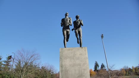 Two-statues-of-runners-mid-stride-on-a-pedestal,-blue-sky-background-in-Vancouver