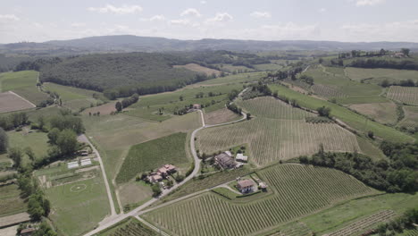 Drone-shot-of-winding-roads-and-golden-farm-fields-in-Tuscany-Italy-landscape-on-a-sunny-day-with-blue-sky-and-clouds-on-the-horizon-LOG