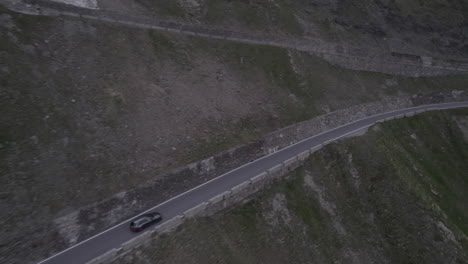 Drohnenaufnahme-Eines-Autos,-Das-An-Einem-Grauen-Tag-Mit-Schnee-Auf-Den-Bergen-Auf-Einem-Kurvenreichen-Straßenprotokoll-Den-Hügel-Am-Stilfser-Joch-In-Italien-Hinauffährt