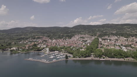 Drone-shot-flying-over-Lake-Bolsena-in-Italy-coming-from-the-water-into-the-old-medieval-city-with-a-castle-and-old-buildings-on-the-hill-and-a-small-harbour-on-a-sunny-day-LOG