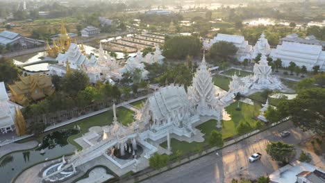 Aerial-of-Wat-Rong-Khun-the-giant-buddhist-White-Temple-and-Golden-Temple-with-mountains-and-landscape-in-Chiang-Rai,-Thailand