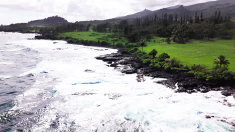 Schnelles-Schwenkvideo-Aus-Der-Luft-Von-Durchscheinenden-Blauen-Wellen,-Die-An-Einem-Heißen-Und-Feuchten-Tag-Während-Einer-Küstenwanderung-Auf-Der-Insel-über-Die-Scharfe-Und-Zerklüftete-Felswand-In-Hawaii-Krachen