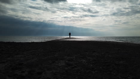 Man-in-a-black-coat-leaving-the-jetty,-walking-towards-camera,-away-from-the-horizon