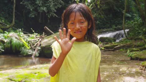 Young-girl-waving-in-the-lush-greenery-of-Pucallpa,-Peru,-with-natural-joy-and-a-waterfall-backdrop