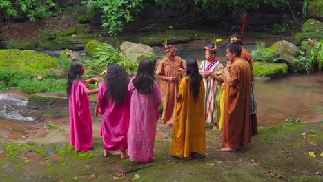 Indigenous-people-in-traditional-dress-by-a-stream-in-Oxapampa,-Peru,-sharing-stories-and-culture,-surrounded-by-lush-greenery