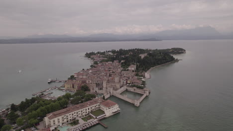 Drone-shot-of-Simione-Italy-looking-over-the-old-fortress-on-a-grey-day-with-boats-around-in-the-water-near-the-lake-LOG