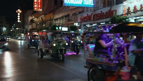 Late-Night-Tuk-Tuk-Taxis-Transporting-Foreign-Tourists-Visiting-The-Chinatown-Night-Market-In-Bangkok-Thailand