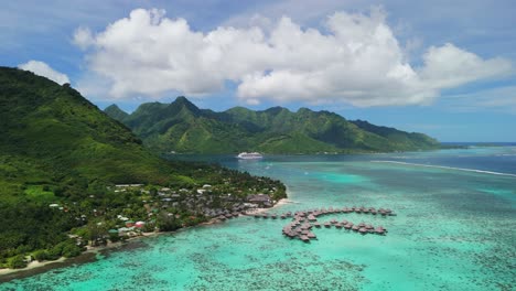 Aerial-flight-with-overwater-bungalow-along-the-coastline-of-Moorea,-French-Polynesia-and-cruise-ship-in-the-background