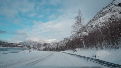 POV-footage-of-a-winter-drive,-showcasing-snowy-mountain-roads-and-the-stunning-view-of-fjords-under-a-clear-blue-sky
