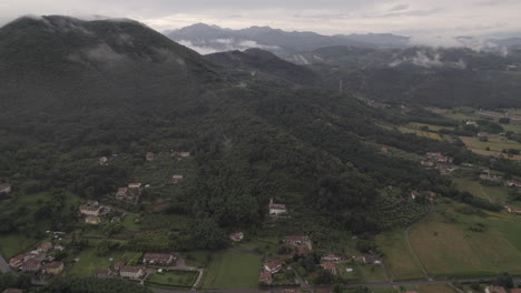 Drone-timelapse-of-clouds-moving-past-the-camera-in-the-hills-and-mountains-in-Italy-on-a-cloudy-grey-day-with-villages-and-houses-down-on-the-ground-in-between-green-fields-LOG