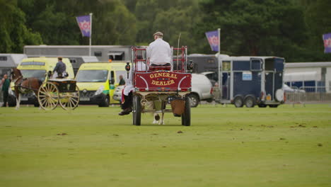 Carriage-races-along-polo-field-during-driving-competition,-the-carriage-is-red-with-writing-on-the-back