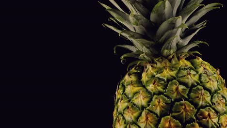 Pineapple-spins-slowly-as-water-droplet-drips-down-on-golden-skin-on-black-background