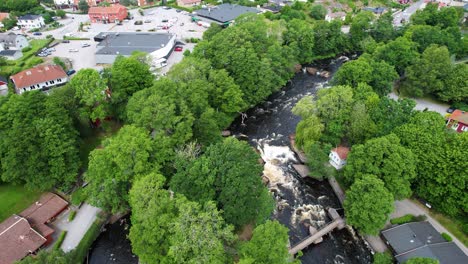 Closing-in-on-Morrum-River-in-Morrum-Town,-Sweden,-with-greenery-and-buildings,-Aerial