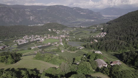 Drone-shot-from-Tesimo-Italy-looking-over-the-valley-of-Bozen-in-between-the-hills-and-mountains-on-a-sunny-but-cloudy-day-with-clouds-LOG