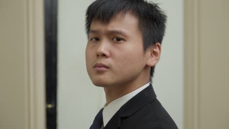 Junger-Asiatischer-Geschäftsmann-Passt-Seinen-Anzug-An,-Lächelnd,-Nahaufnahme,-Innenbereich