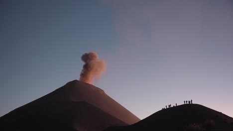 Filmischer-Ausbruch-Am-Vulkan-Fuego:-Silhouettengruppe-Auf-Einem-Bergrücken,-Asche,-Lava-Und-Touristen,-Lebendige-Sonnenuntergangsfarben
