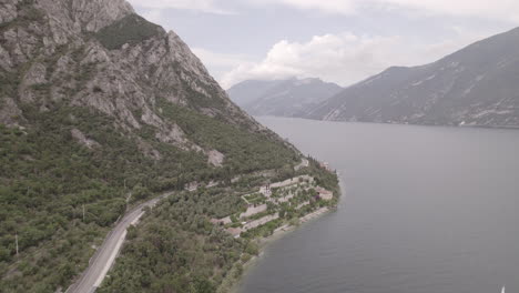 Droneshot-Sobre-La-Ciudad-Limone-Italia-En-El-Lago-De-Garda-En-Un-Día-Gris-Con-Montañas,-Nubes-Y-Troncos-De-Agua