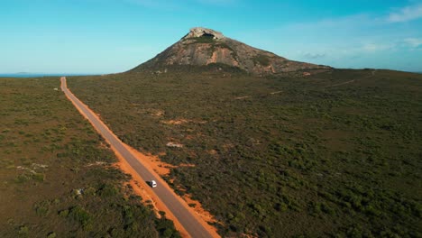 van-driving-on-a-straight-road-in-cape-legrand-national-park-with-frenchman-peak-in-the-background-on-a-sunny-day,-esperance,-western-australia