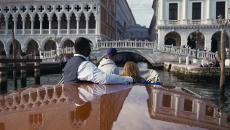 A-mixed-race-couple-having-a-private-boat-trip-through-Venice-italy-and-are-about-to-pass-the-Ponte-della-paglia-bridge-at-Palazzo-Ducale-with-tourists-on-it