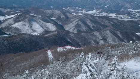 Skiers-Travel-on-Ski-Chair-Lift-Towards-Balwangsan-Mountain-and-Daegwallyeong-Mountains-Chain-Valley-Top-Down-View,-Gangwon-do---aerial-view