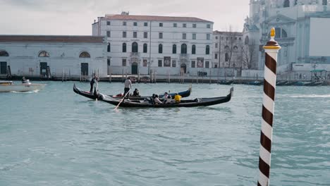Dos-Góndolas-Tradicionales-Flotando-Con-Turistas-En-Un-Recorrido-Turístico-Con-Los-Gondoleros-En-El-Gran-Canal-De-Venecia,-Italia,-Frente-A-La-Basílica-De-Santa-María-Della-Salute.