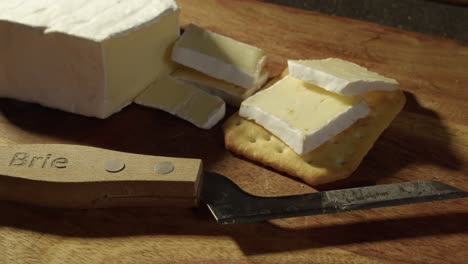 Close-up-slices-of-Brie-cheese-put-onto-soda-cracker,-knife-on-board
