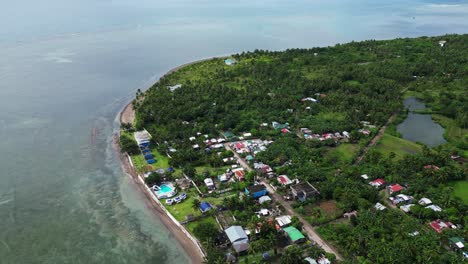 Stunning-overhead-view-of-rural,-island-village-with-lush-jungles-facing-clear-ocean-coastline-in-Catanduanes,-Philippines