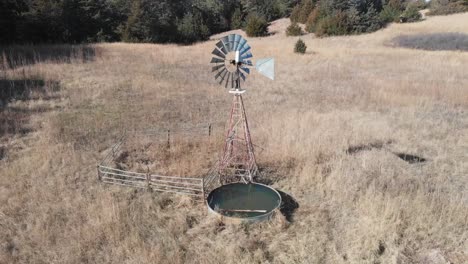Drone-shot-as-it-circles-around-a-windmill-shifting-in-the-wind-near-the-coniferous-forest-in-Nebraska-on-a-sunny-day