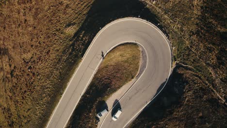 Aerial-view-of-a-winding-road-with-a-cyclist-and-cars,-surrounded-by-rugged-terrain