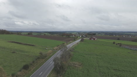 Drohnenaufnahme-Einer-Belgischen-Landschaft-An-Einem-Grauen-Tag-Mit-Sich-Schnell-Bewegenden-Wolken-Und-Einer-Straße-Und-Einem-Dorf-Im-Hintergrund