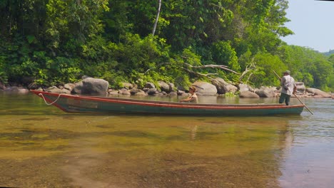 Two-locals-navigating-a-canoe-in-the-clear-waters-of-Oxapampa,-Peru,-surrounded-by-lush-greenery