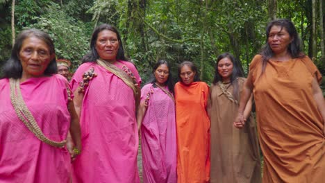 Mujeres-Indígenas-Con-Atuendos-Vibrantes-Caminando-Por-Un-Frondoso-Bosque,-Tomadas-De-La-Mano,-En-Oxapampa,-Perú.