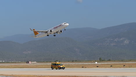 Pegasus-airbus-a321-airplane-leaving-Antalya-runway-with-yellow-vehicle-driving-alongside,-Slow-motion