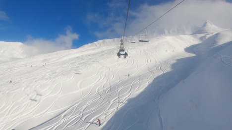 Two-Man-Chairlift-First-Person-View-Ascending-on-Sunny-Blue-Sky-Day-with-Ski-Tracks-in-Powder-and-Skiers-Below