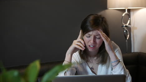 Sad-and-upset-young-professional-woman-receiving-bad-news-on-the-phone-at-home-working-on-laptop