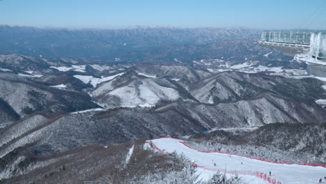 Monapark-Rooftop-View-on-Skiers-Skiing-Down-the-Hill-of-Balwangsan-Mountain-Ski-Slope-in-Yong-Pyong-Ski-Resort-Pyeongchang-gun-and-Daegwallyeong-Mountain-Chain---Aerial-High-Angle-Skyline