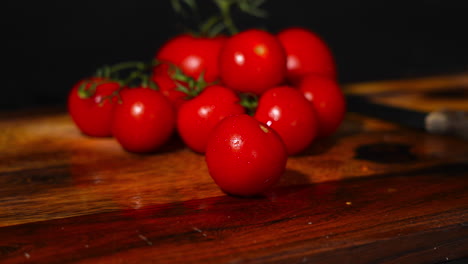Handheld-shot-of-a-tomato-falling-on-a-wooden-cutting-board-with-a-stack-of-tomatoes-in-the-background