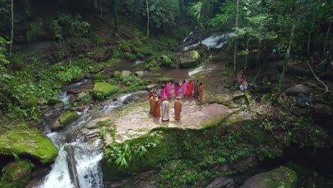 Indigenous-people-in-traditional-attire-dancing-in-a-circle-by-a-waterfall-in-pucallpa,-peru,-aerial-view