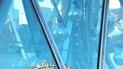 Giant-Ferris-wheel-reflected-in-glass-building-under-clear-blue-sky,-architecture,-amusement-ride