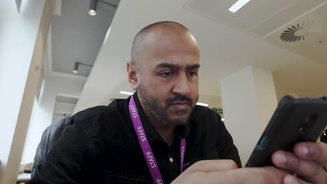 Man-in-black-shirt-using-smartphone-indoors,-focused-expression,-office-environment