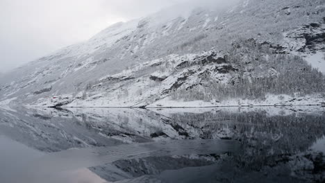 POV-footage-of-a-boat-ride-through-Geirangerfjord,-Norway,-highlighting-the-fjord's-tranquil-beauty-and-the-surrounding-snowy-mountains-in-winter