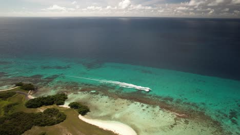 Ein-Boot,-Das-Im-Klaren-Türkisfarbenen-Wasser-In-Der-Nähe-Der-üppig-Grünen-Inseln-Los-Roques,-Venezuela,-Fährt,-Luftaufnahme
